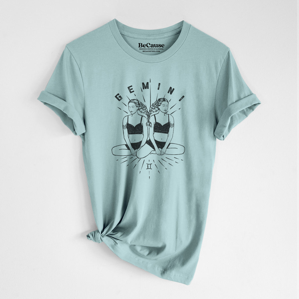 Dusty blue lightweight cotton t-shirt laid flat with the sleeves rolled, printed with black ink twin women sitting back to back with the word Gemini, for the Gemini zodiac sign.