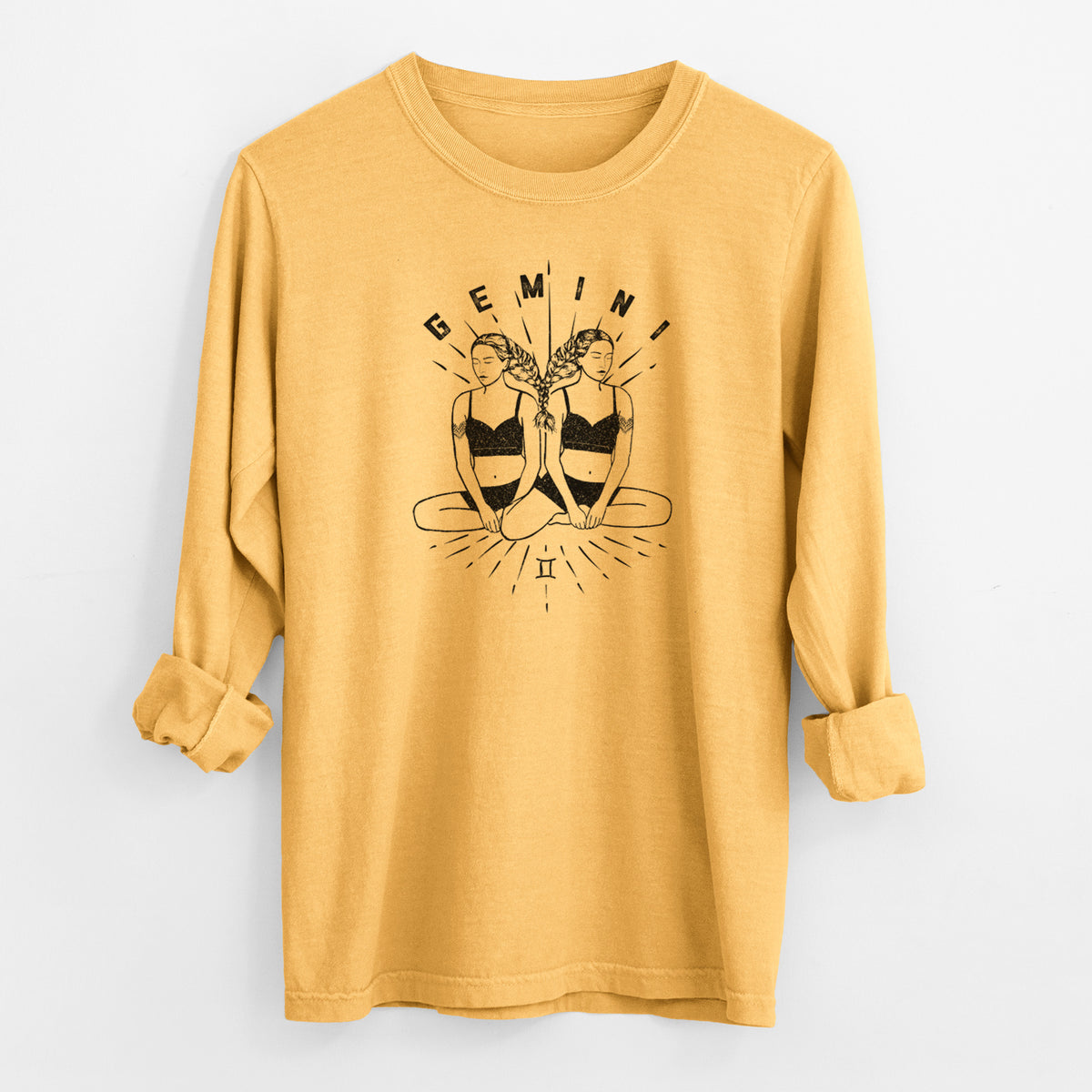 Golden wheat yellow Comfort Colors long sleeve shirt laid flat with the cuffs rolled, printed with black ink twin women sitting back to back with the word Gemini, for the Gemini zodiac sign.