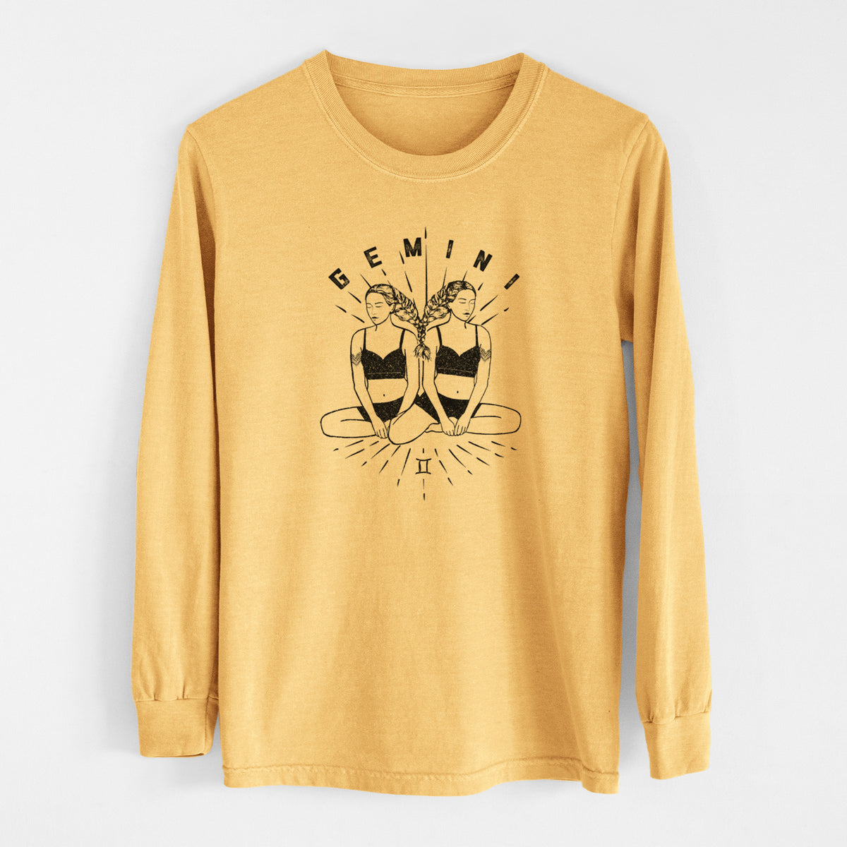 Golden wheat yellow Comfort Colors long sleeve shirt laid flat, printed with black ink twin women sitting back to back with the word Gemini, for the Gemini zodiac sign.