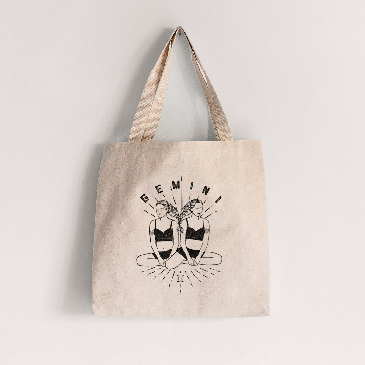 Natural canvas tote bag printed with black ink twin women sitting back to back with the word Gemini, for the Gemini zodiac sign.