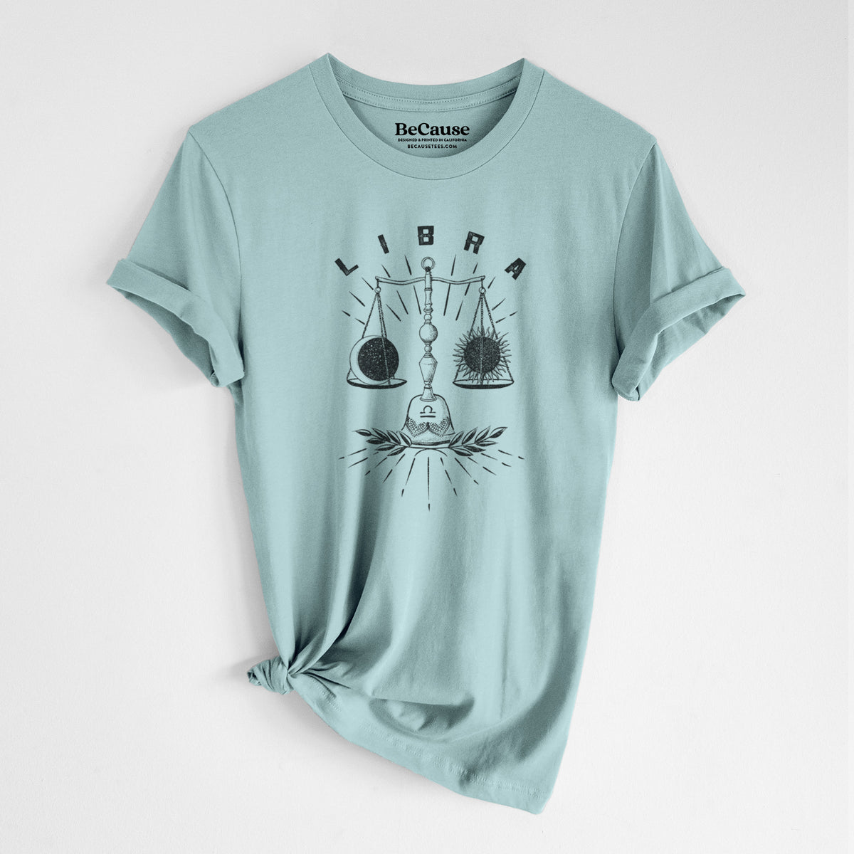 Dusty blue lightweight cotton t-shirt laid flat with the sleeves rolled, printed with a black ink set of balance scales with the word Libra, for the Libra zodiac sign.