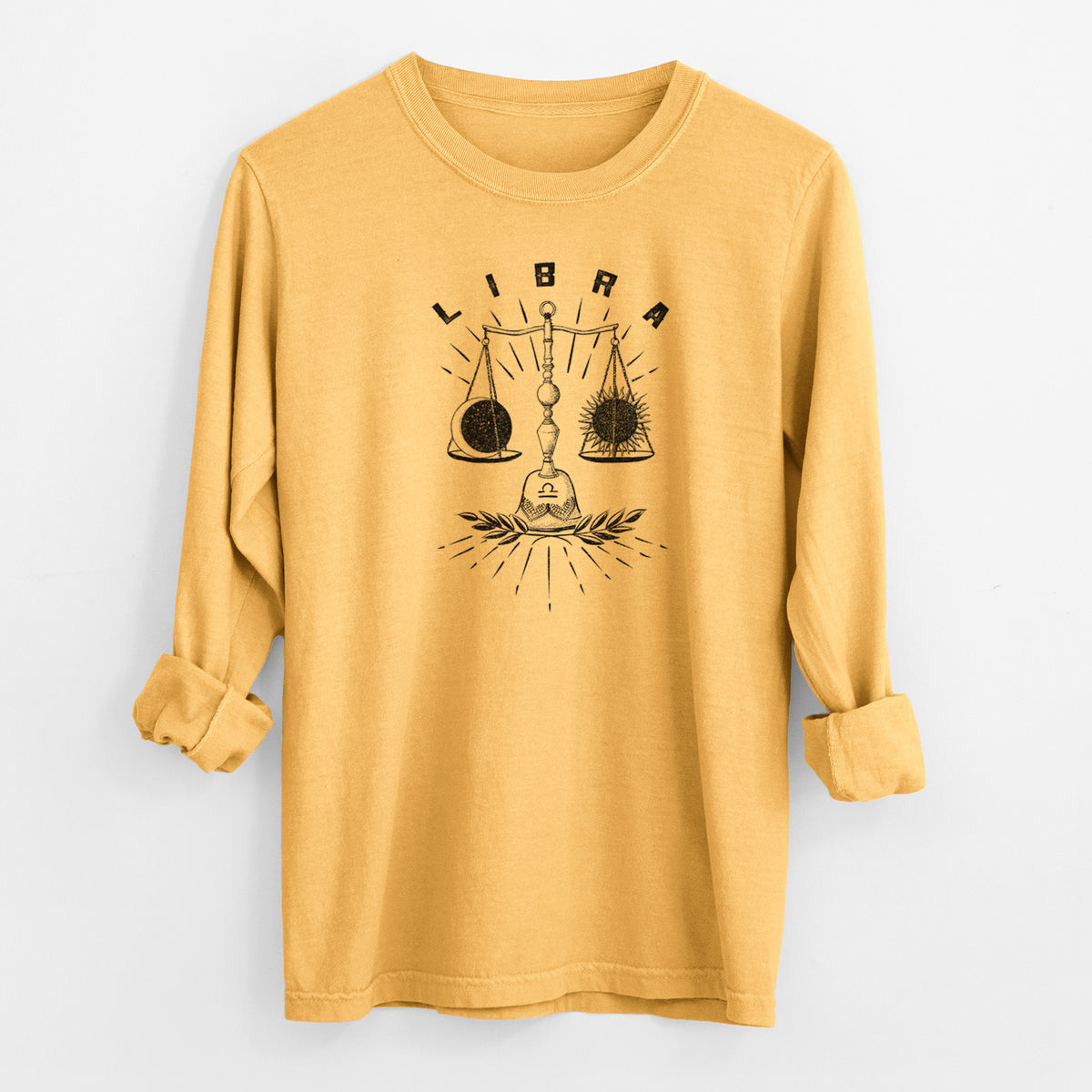 Golden wheat yellow Comfort Colors long sleeve shirt laid flat with the cuffs rolled, printed with a black ink set of balance scales with the word Libra, for the Libra zodiac sign.