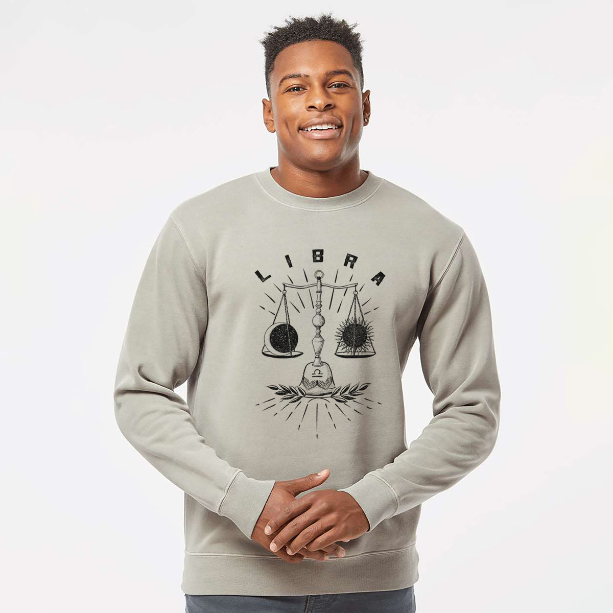 Model wearing a cement grey pigment dyed crewneck sweatshirt printed with a black ink set of balance scales with the word Libra, for the Libra zodiac sign.