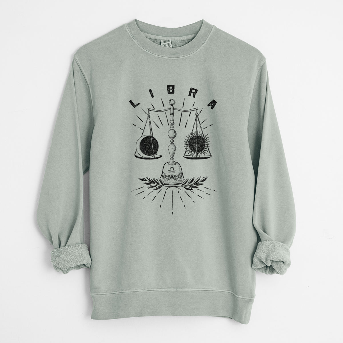 Sage green pigment dyed crewneck sweatshirt laid flat with the sleeves rolled, printed with a black ink set of balance scales with the word Libra, for the Libra zodiac sign.
