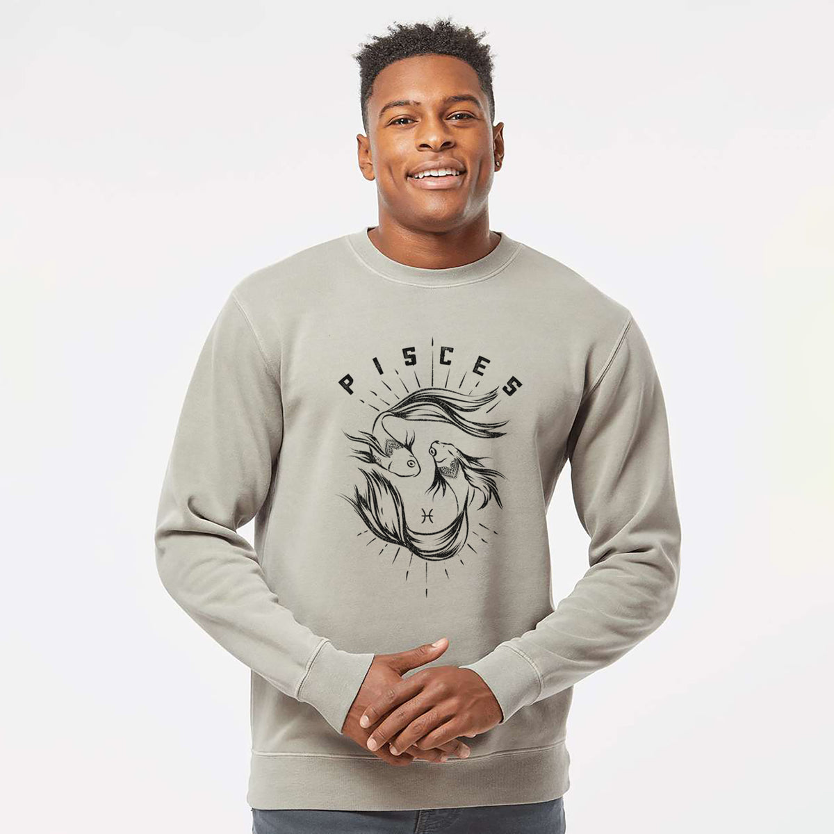 Model wearing a cement grey pigment dyed crewneck sweatshirt printed with two black ink fish swimming in a circle with the word Pisces, for the Pisces zodiac sign.