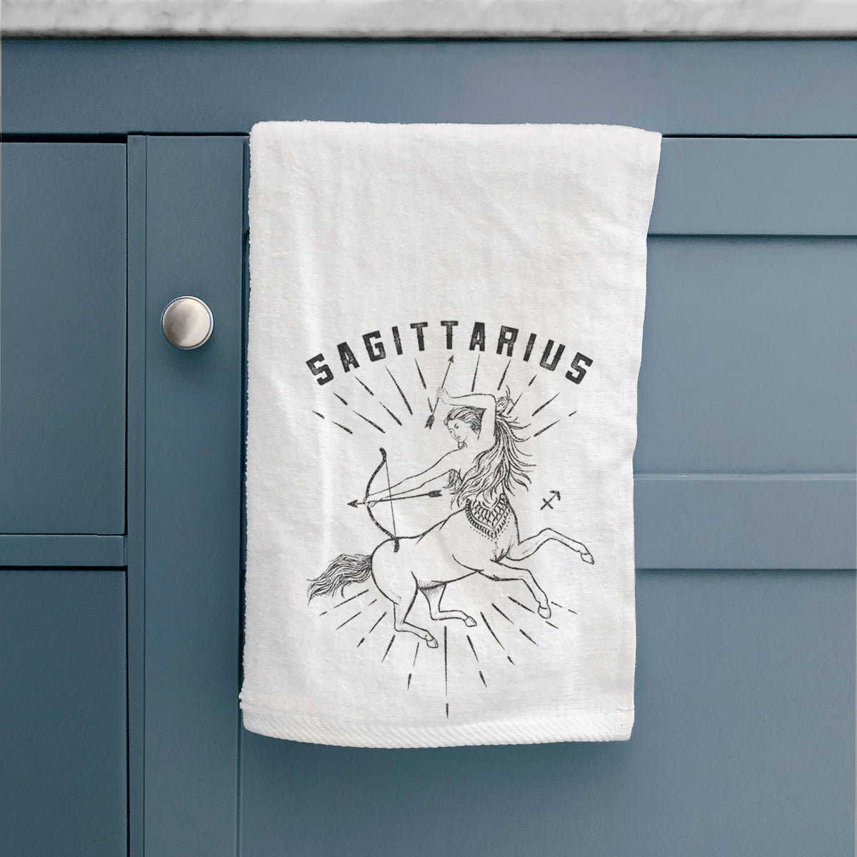 White hand towel printed with a black ink centaur archer with the word Sagittarius, for the Sagittarius zodiac sign, hanging on a cabinet door.