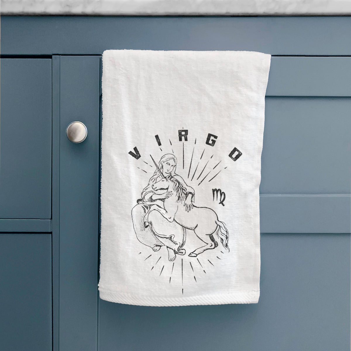 White hand towel printed with a black ink woman holding wheat with the word Virgo, for the Virgo zodiac sign, hanging on a cabinet door.
