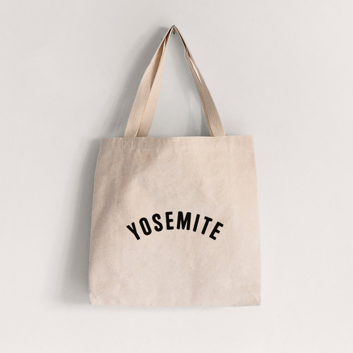 Natural canvas tote bag printed with the word Yosemite in bold black letters arched across the chest.