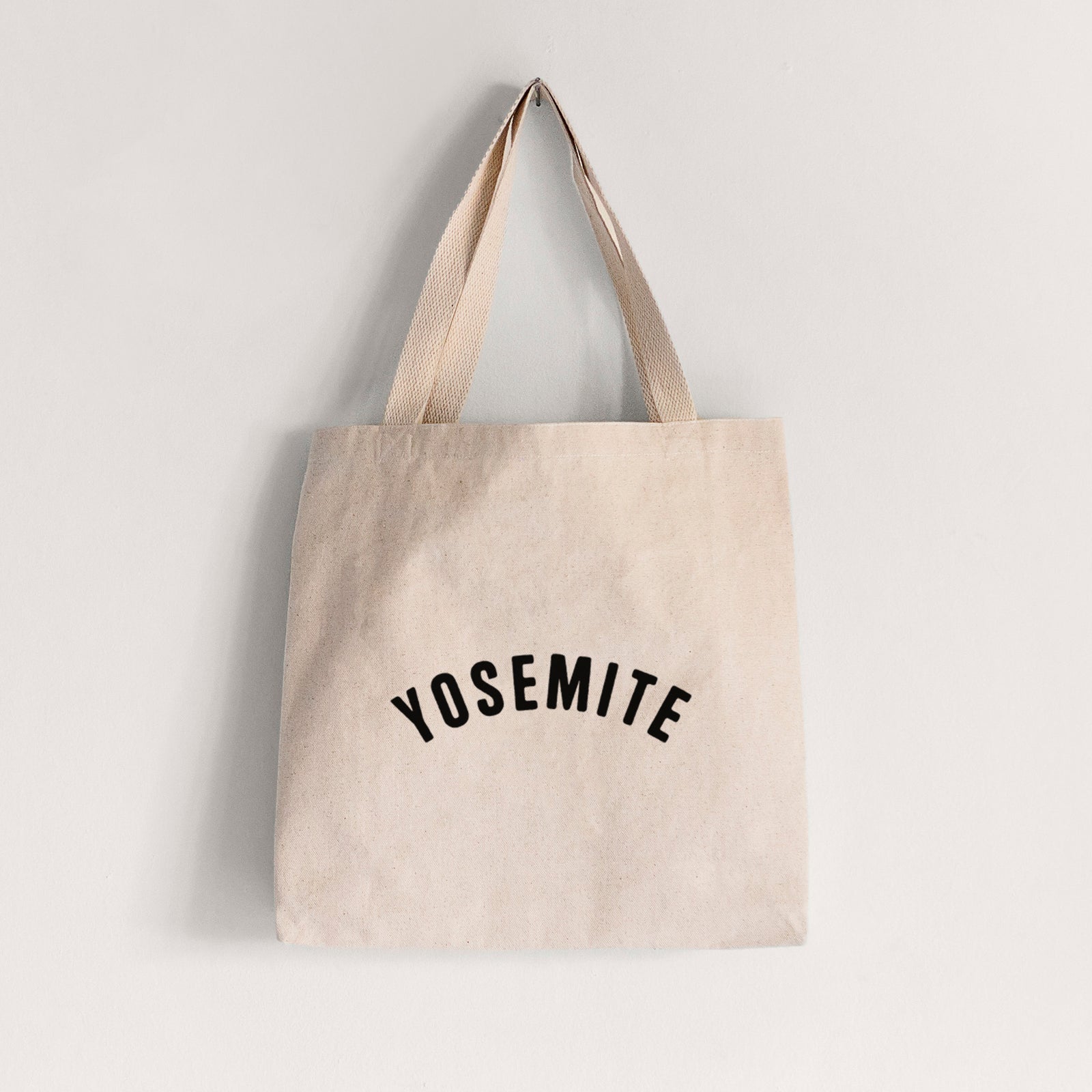 Natural canvas tote bag printed with the word Yosemite in bold black letters arched across the chest.