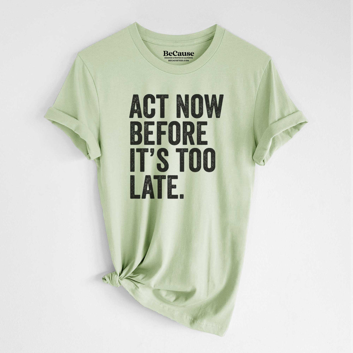 Spring green lightweight cotton t-shirt laid flat with the sleeves rolled, printed with bold black words reading Act Now Before It's Too Late.