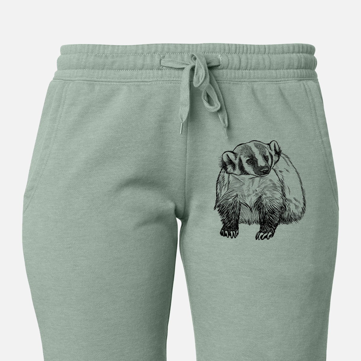 Front of sage green Cali Wave sweatpants, printed with a detailed black ink illustration of an American badger facing forward on the leg.