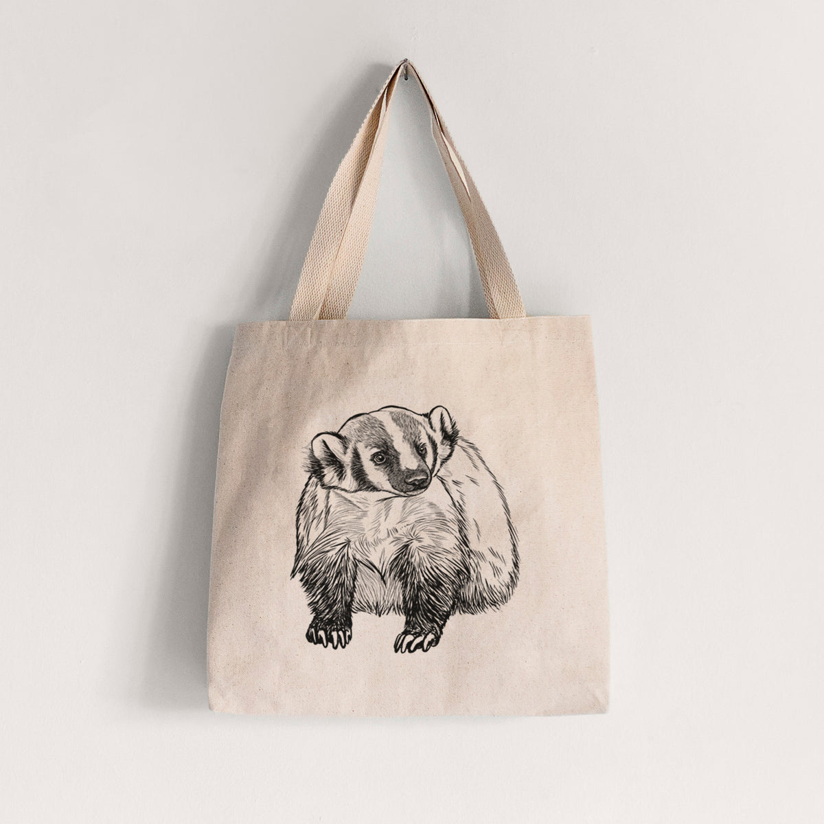 Natural canvas tote bag printed with a detailed black ink illustration of an American badger facing forward.