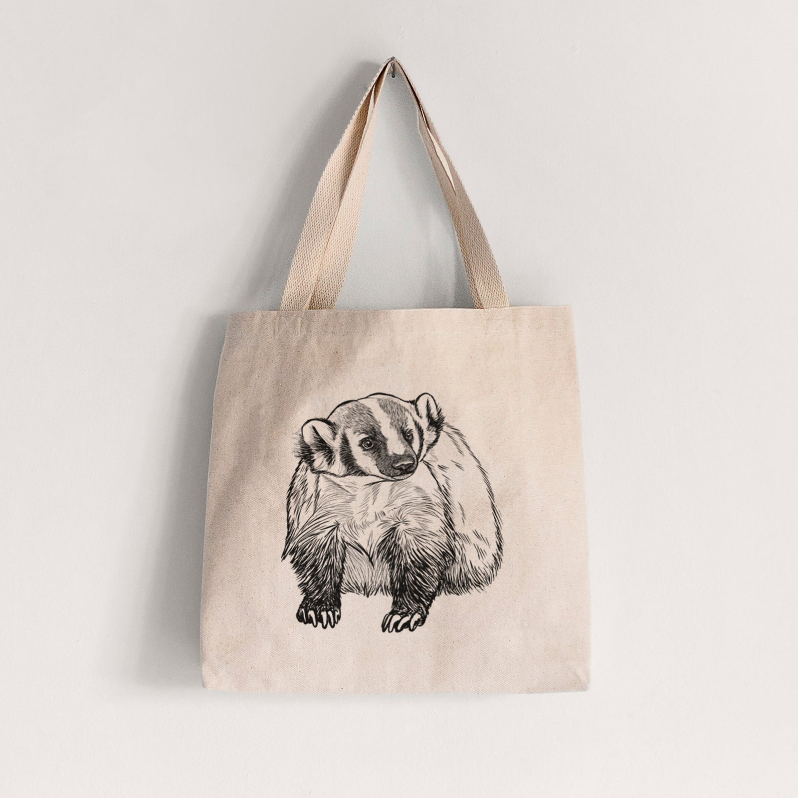 Natural canvas tote bag printed with a detailed black ink illustration of an American badger facing forward.