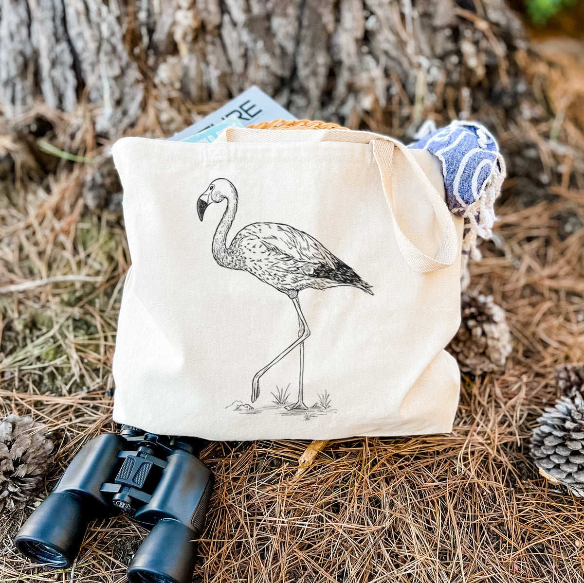 Canvas tote bag printed with a black ink illustration of an Andean flamingo standing on one leg, resting on dry grass beside a pair of binoculars.