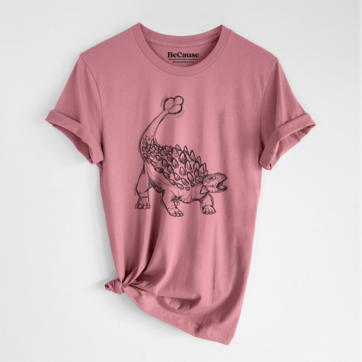 Mauve pink lightweight cotton t-shirt laid flat with the sleeves rolled, printed with a black ink illustration of an Ankylosaurus with its club tail raised.