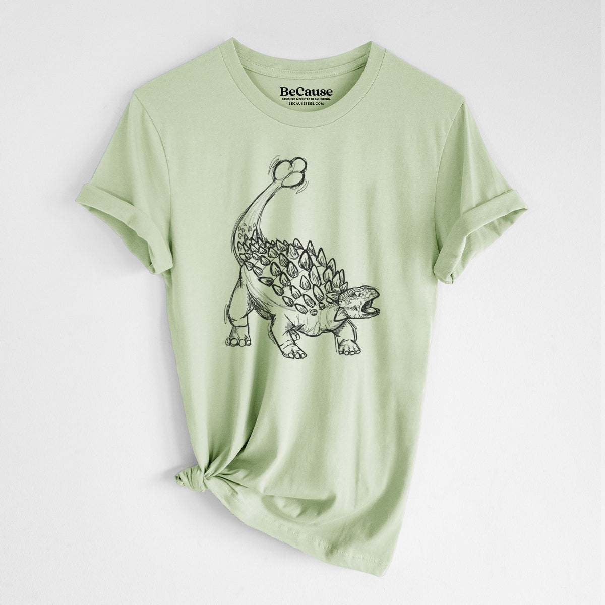 Spring green lightweight cotton t-shirt laid flat with the sleeves rolled, printed with a black ink illustration of an Ankylosaurus with its club tail raised.