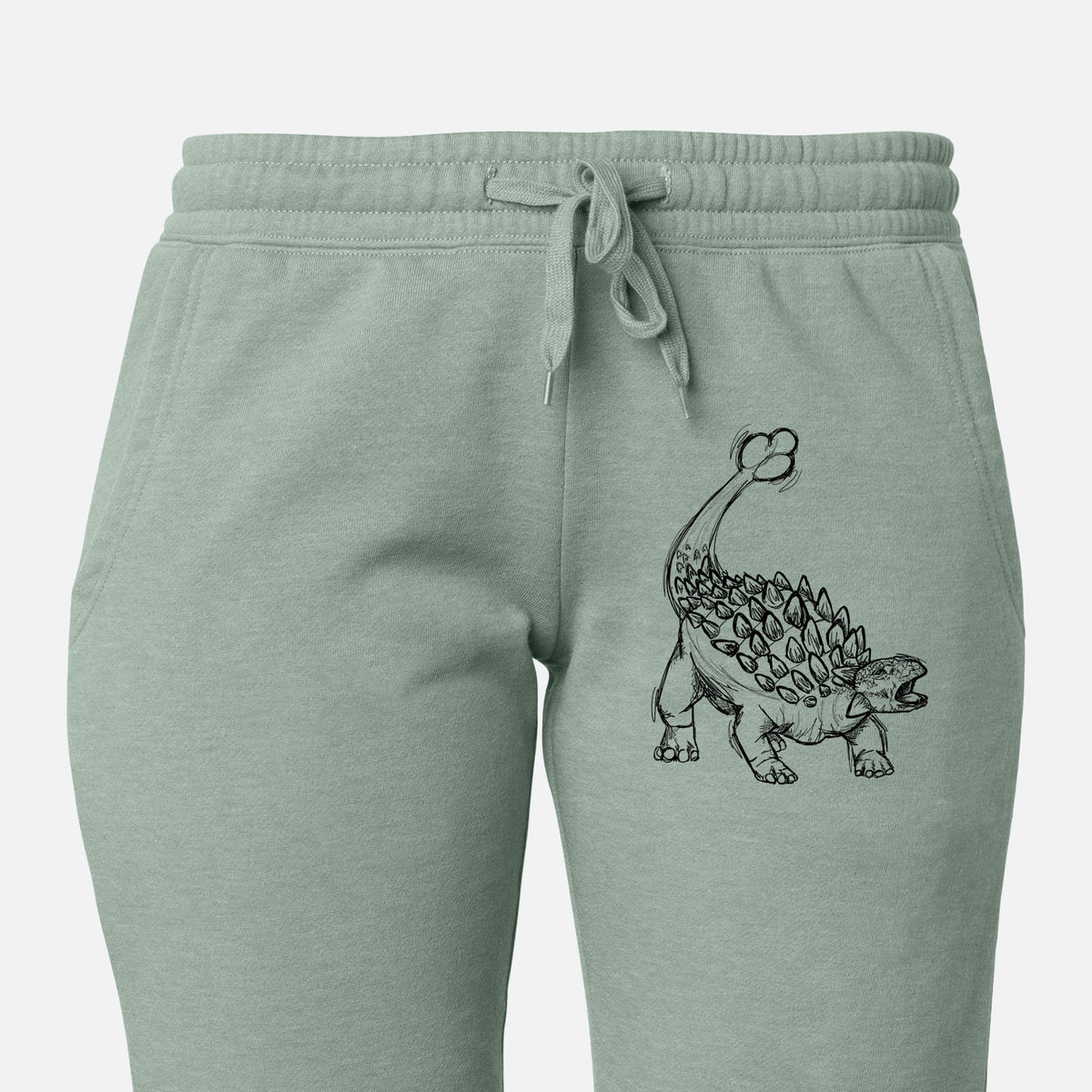 Front of sage green Cali Wave sweatpants, printed with a black ink illustration of an Ankylosaurus with its club tail raised on the leg.