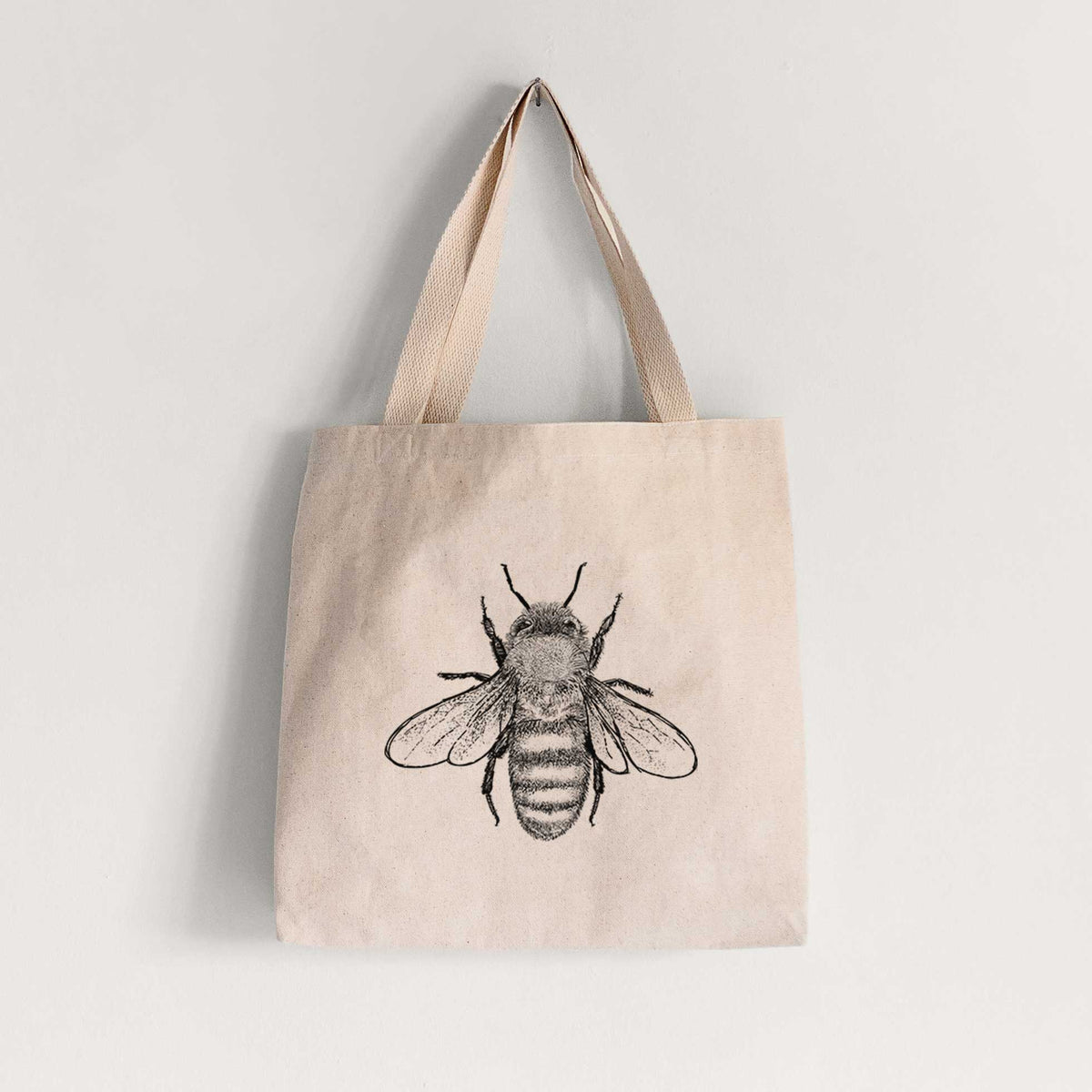 Natural canvas tote bag printed with a detailed black ink illustration of a honey bee with its wings spread, seen from above.