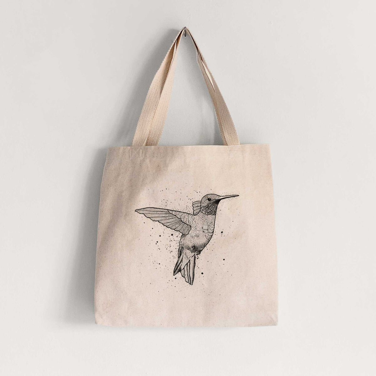 Natural canvas tote bag printed with a black ink sketch of a ruby-throated hummingbird hovering with its wings raised.