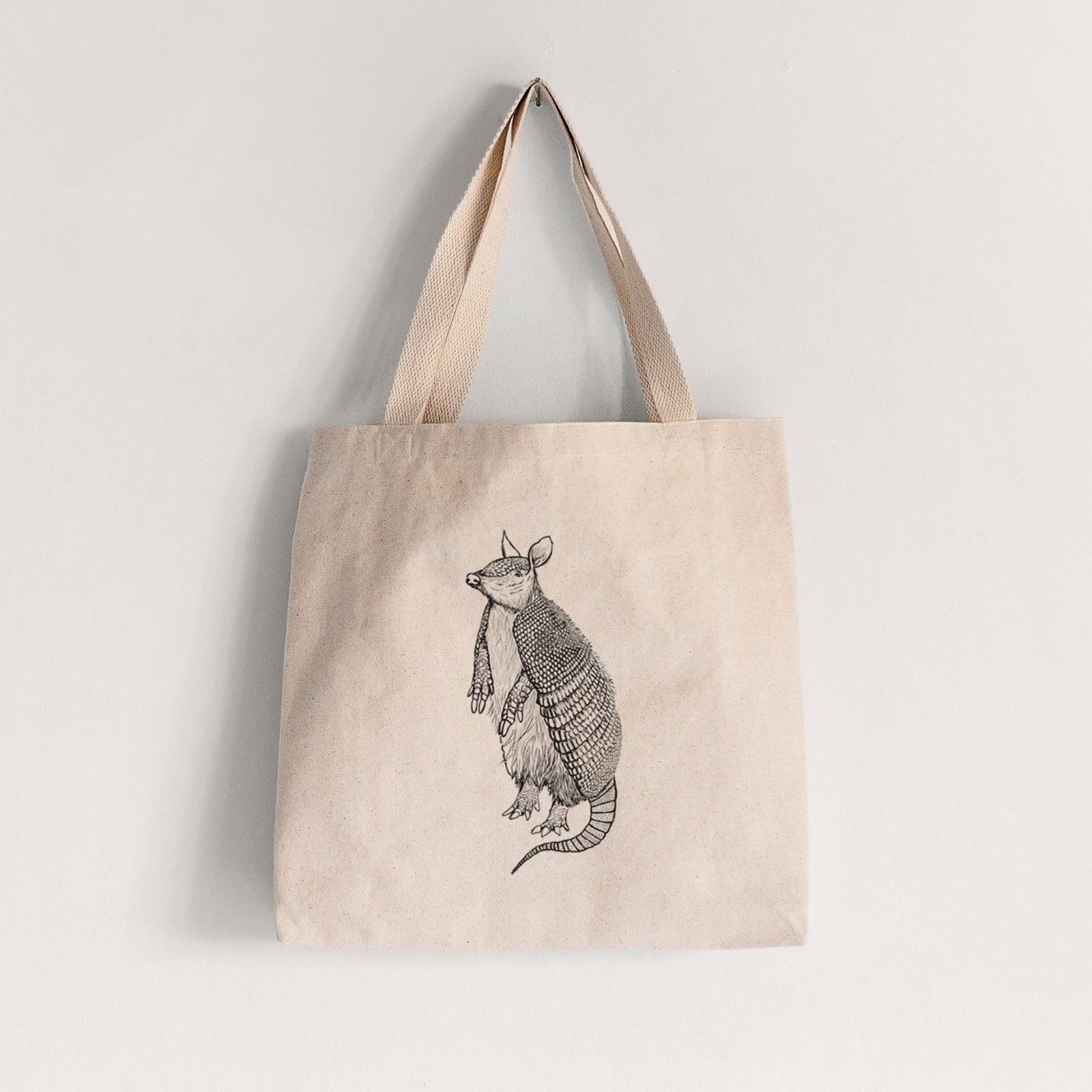 Natural canvas tote bag printed with a black ink illustration of a nine-banded armadillo standing upright.