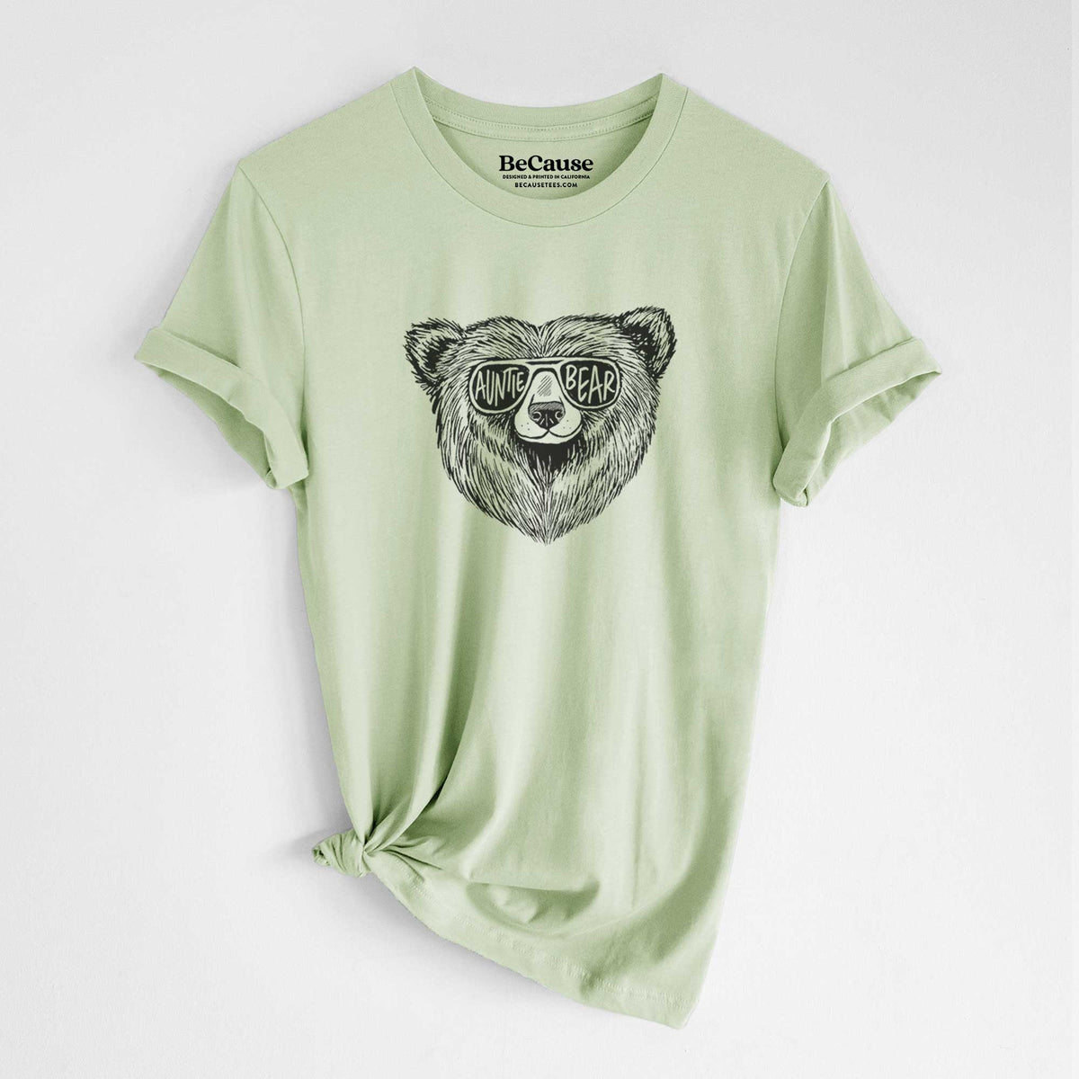Spring green lightweight cotton t-shirt laid flat with the sleeves rolled, printed with a black ink bear's face wearing sunglasses that read Auntie Bear.