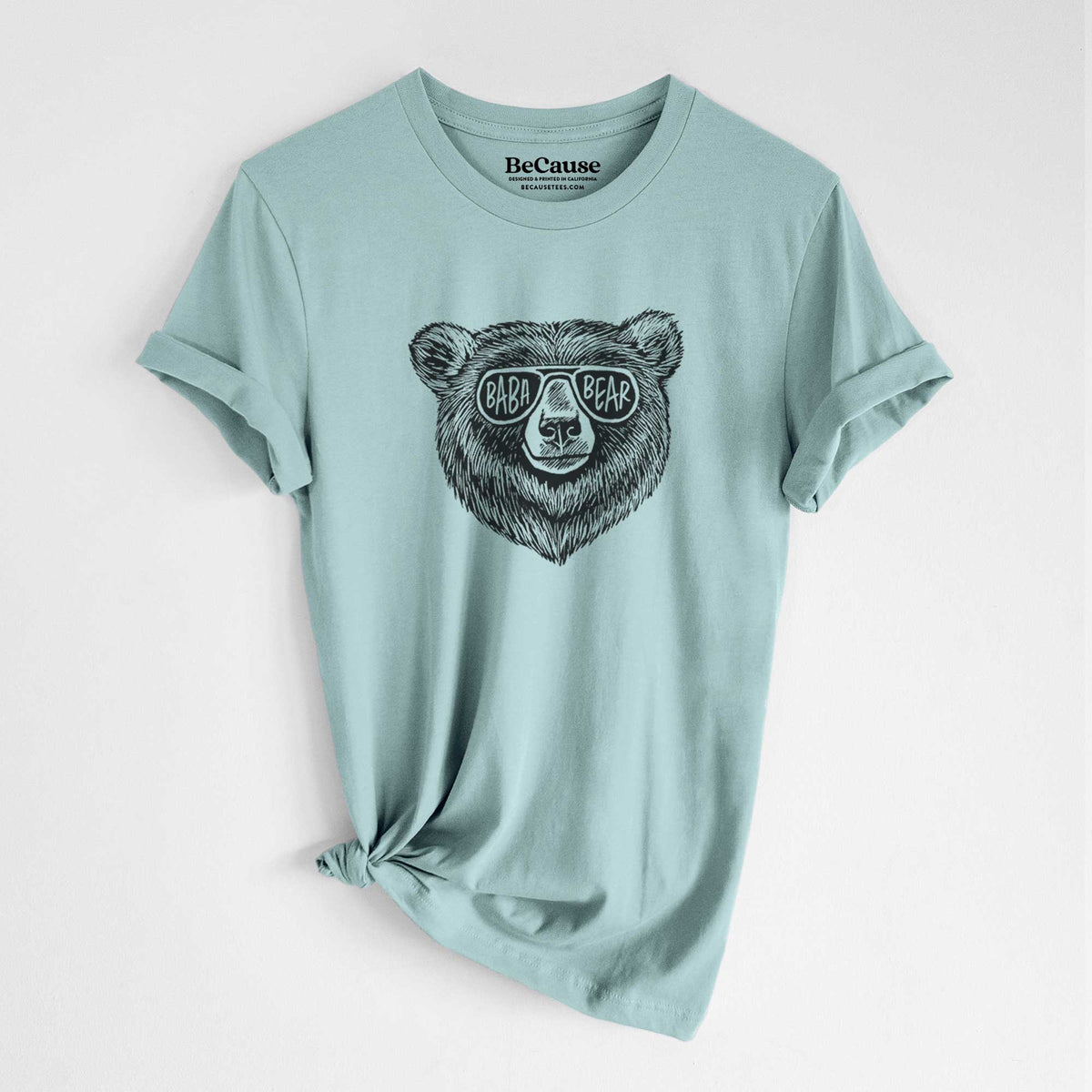 Dusty blue lightweight cotton t-shirt laid flat with the sleeves rolled, printed with a black ink bear's face wearing sunglasses that read Baba Bear.