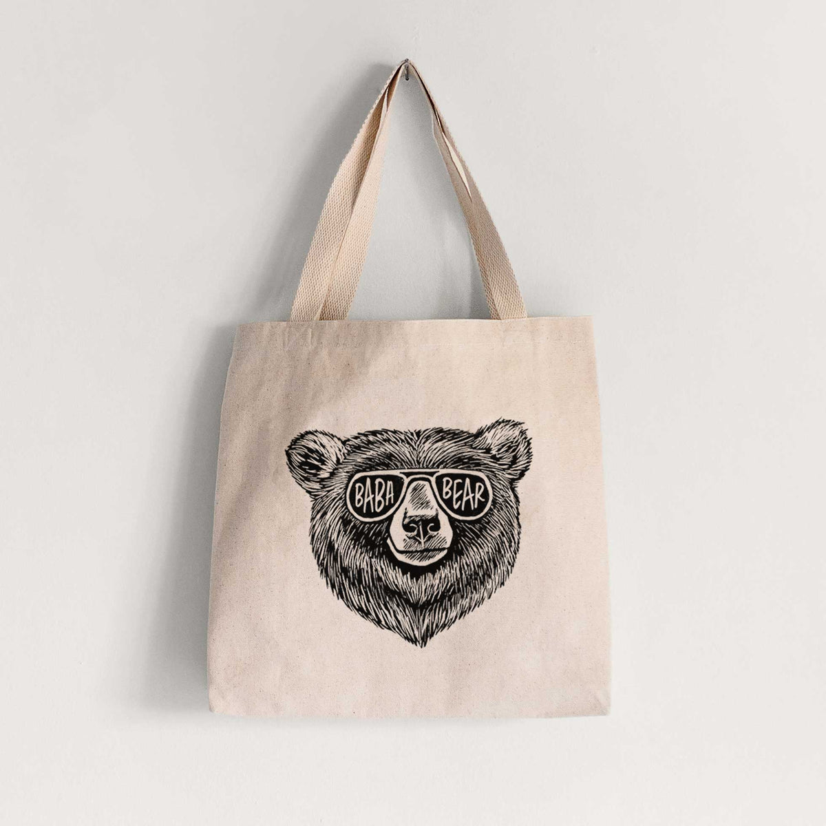 Natural canvas tote bag printed with a black ink bear's face wearing sunglasses that read Baba Bear.