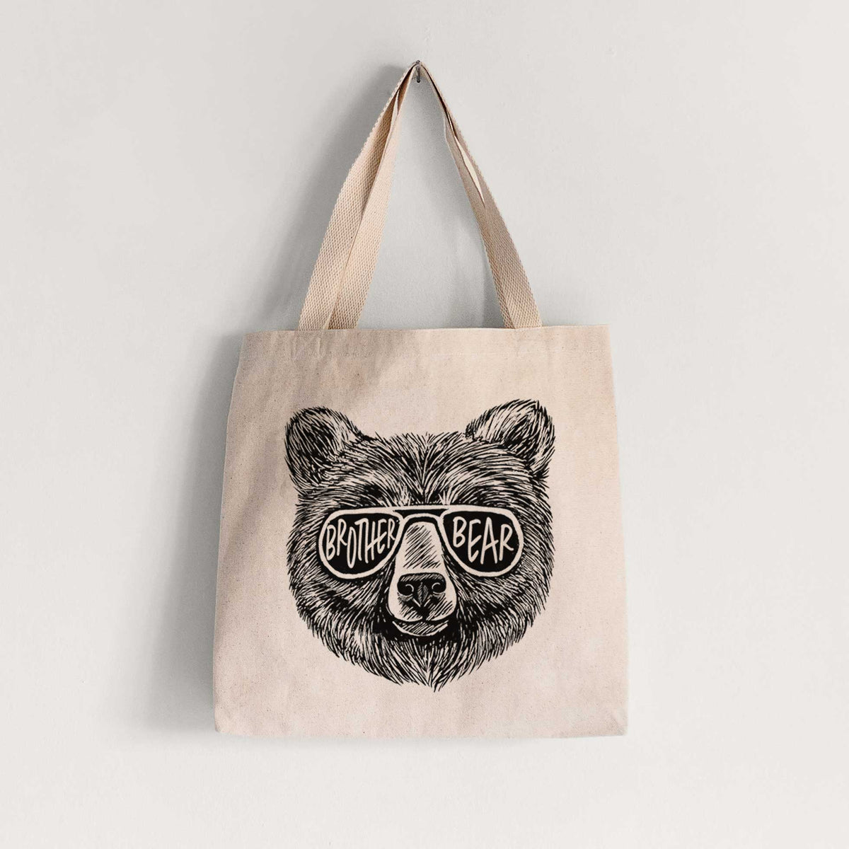 Natural canvas tote bag printed with a black ink bear's face wearing sunglasses that read Brother Bear.