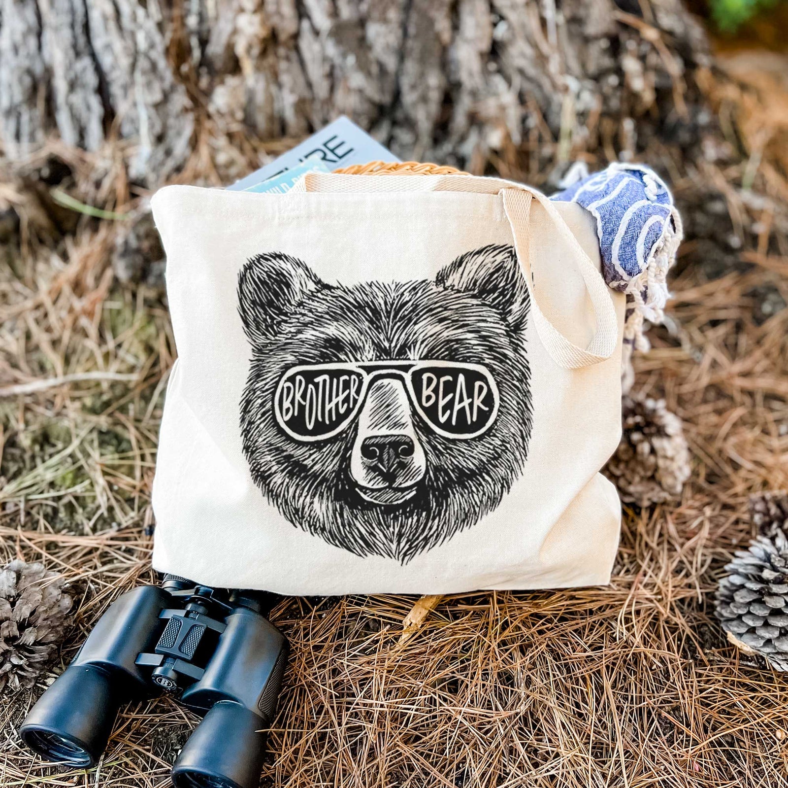 Natural canvas tote bag printed with a black ink bear's face wearing sunglasses that read Brother Bear.