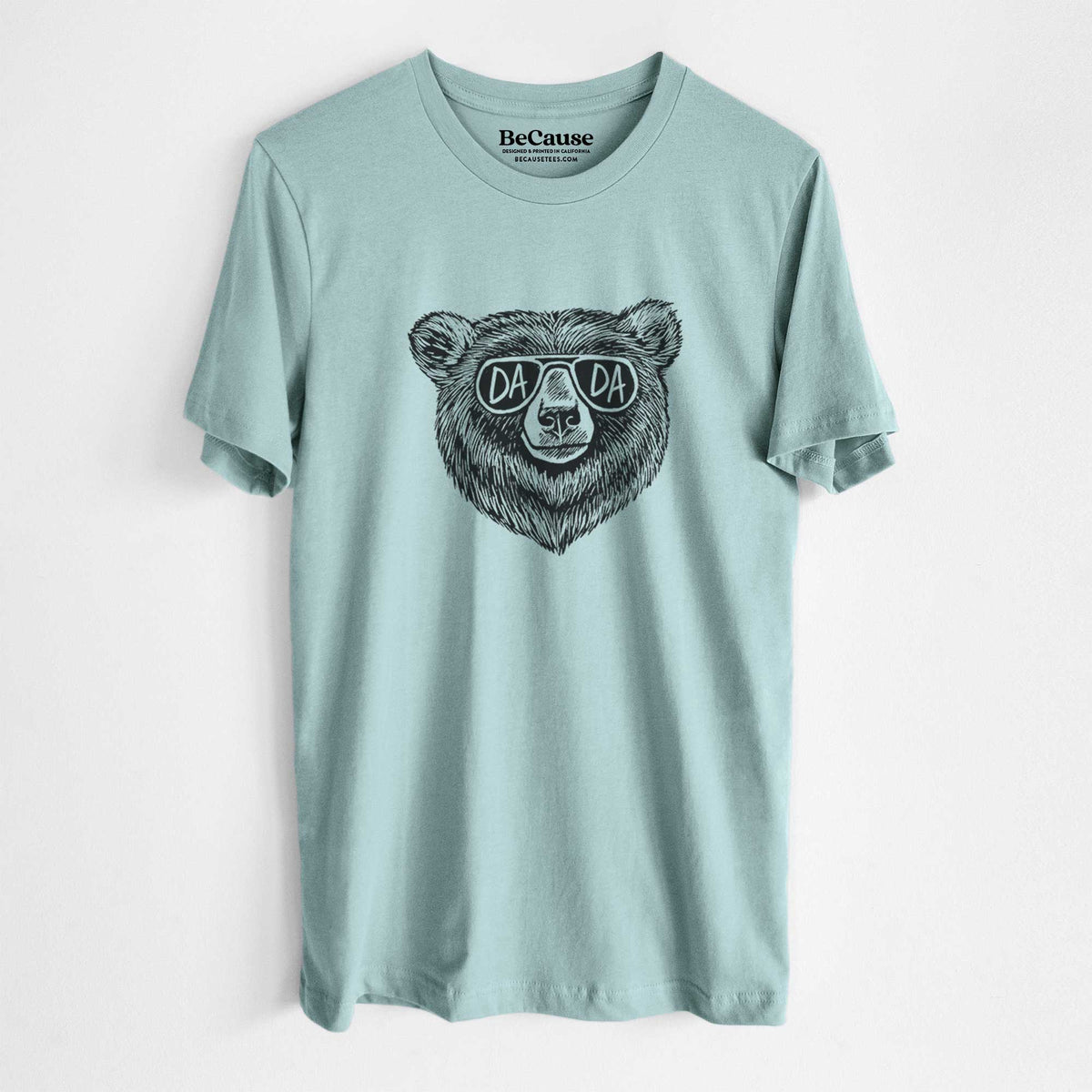 Dusty blue lightweight cotton t-shirt laid flat, printed with a black ink bear's face wearing sunglasses that read Dada.