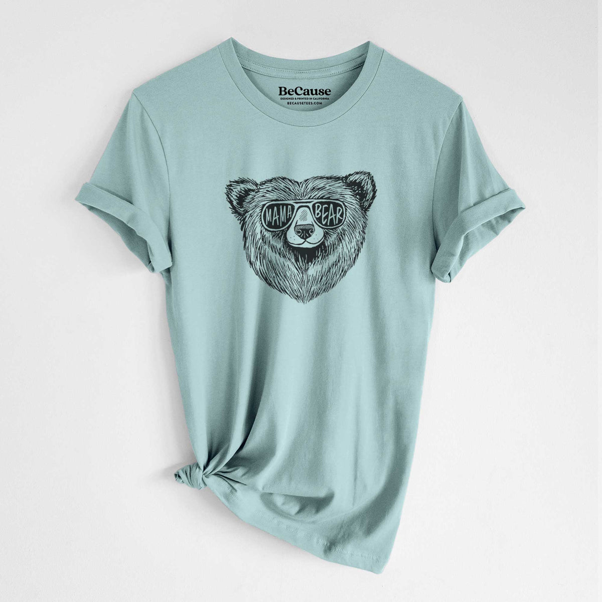 Dusty blue lightweight cotton t-shirt laid flat with the sleeves rolled, printed with a black ink bear's face wearing sunglasses that read Mama Bear.