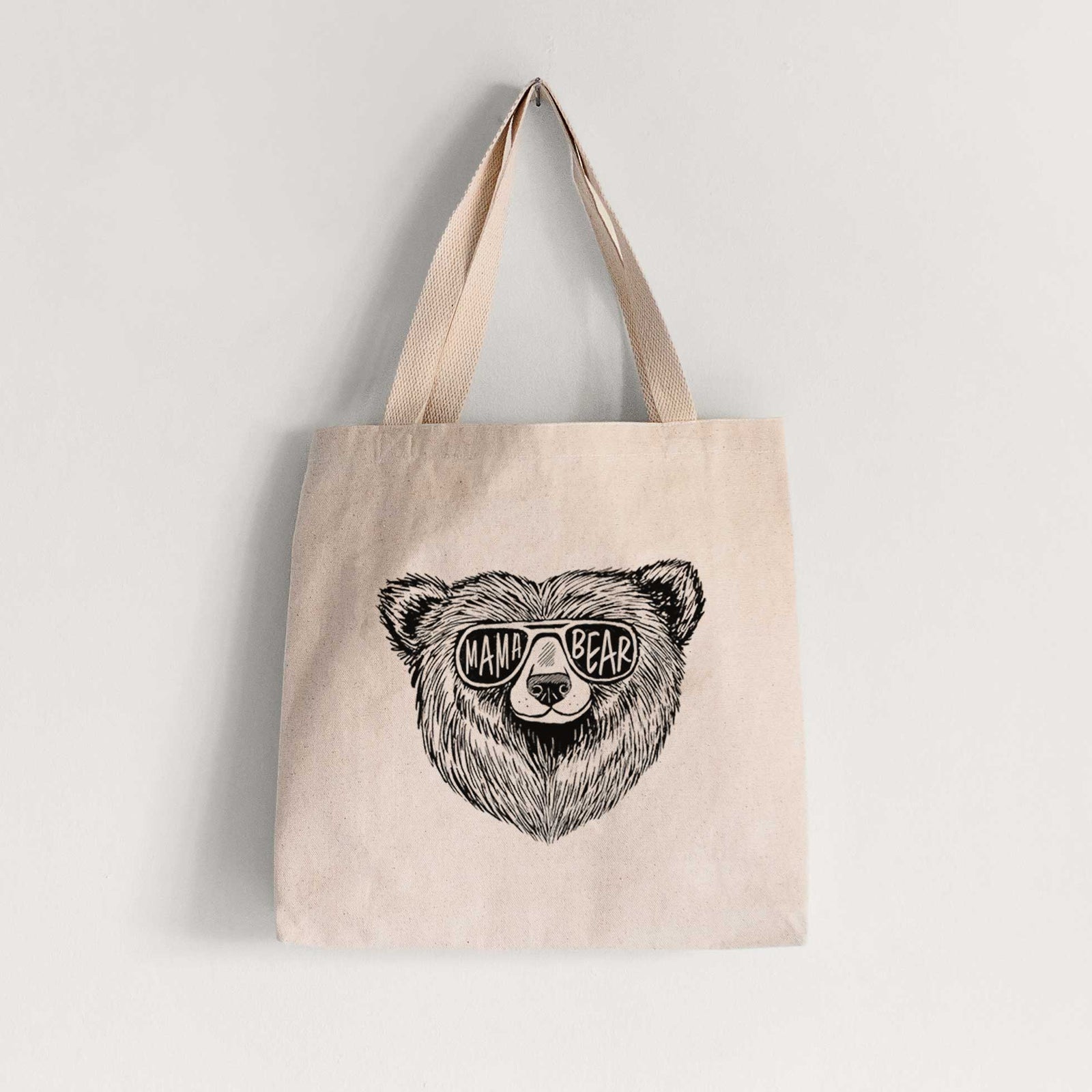 Natural canvas tote bag printed with a black ink bear's face wearing sunglasses that read Mama Bear.