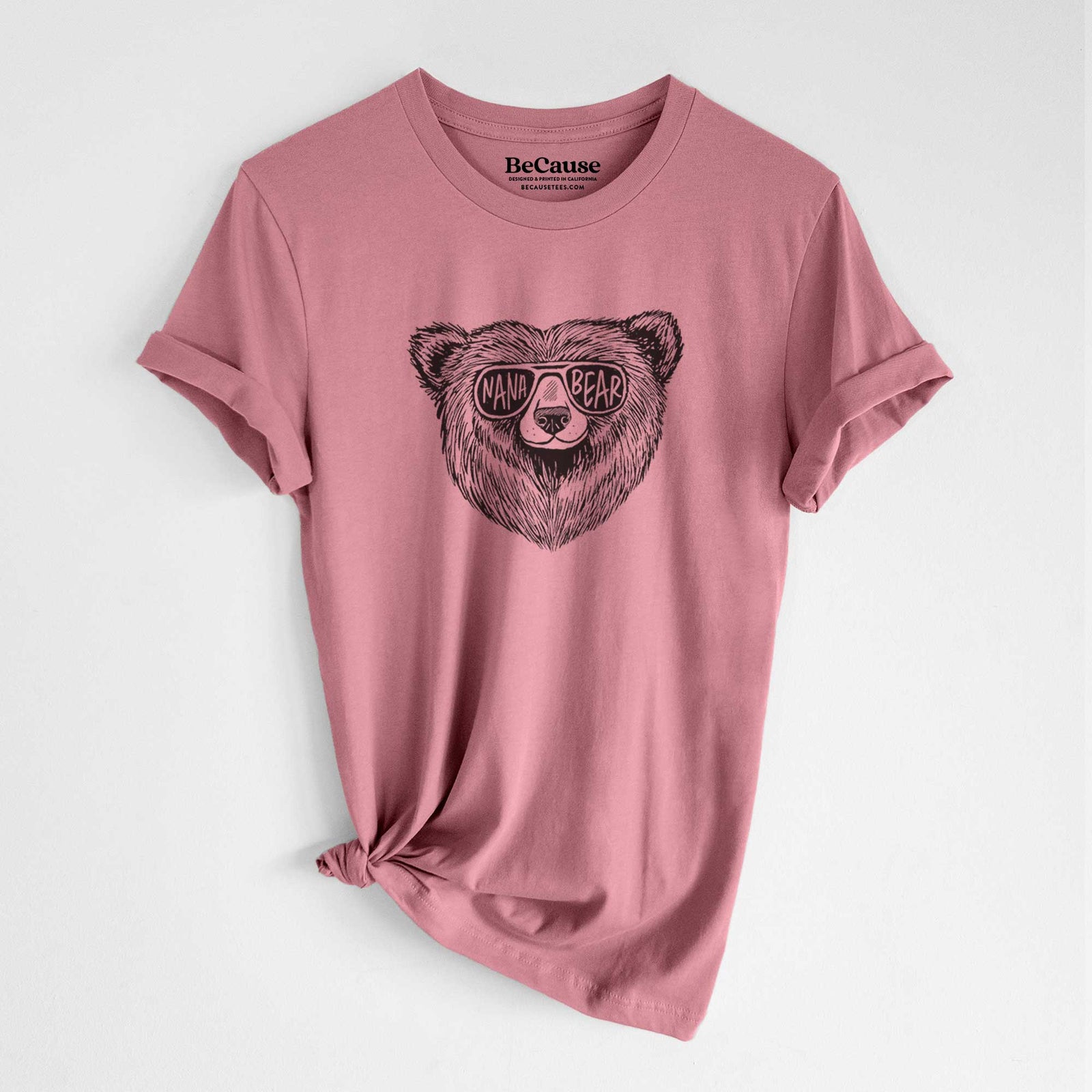 Mauve pink lightweight cotton t-shirt laid flat with the sleeves rolled, printed with a black ink bear's face wearing sunglasses that read Nana Bear.