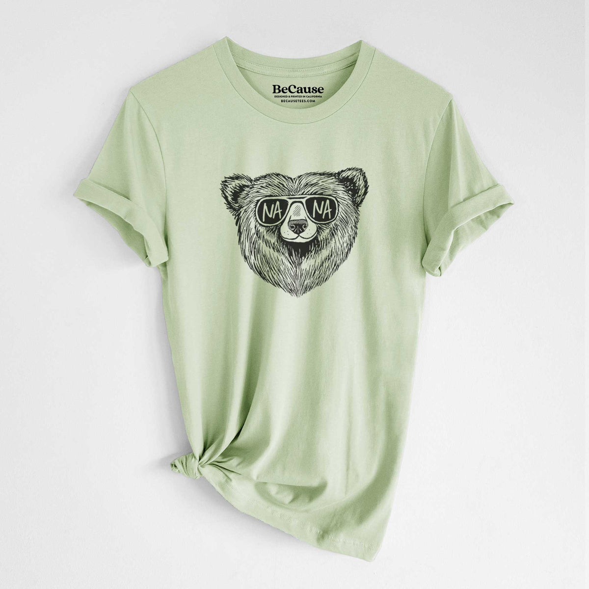 Spring green lightweight cotton t-shirt laid flat with the sleeves rolled, printed with a black ink bear's face wearing sunglasses that read Nana.