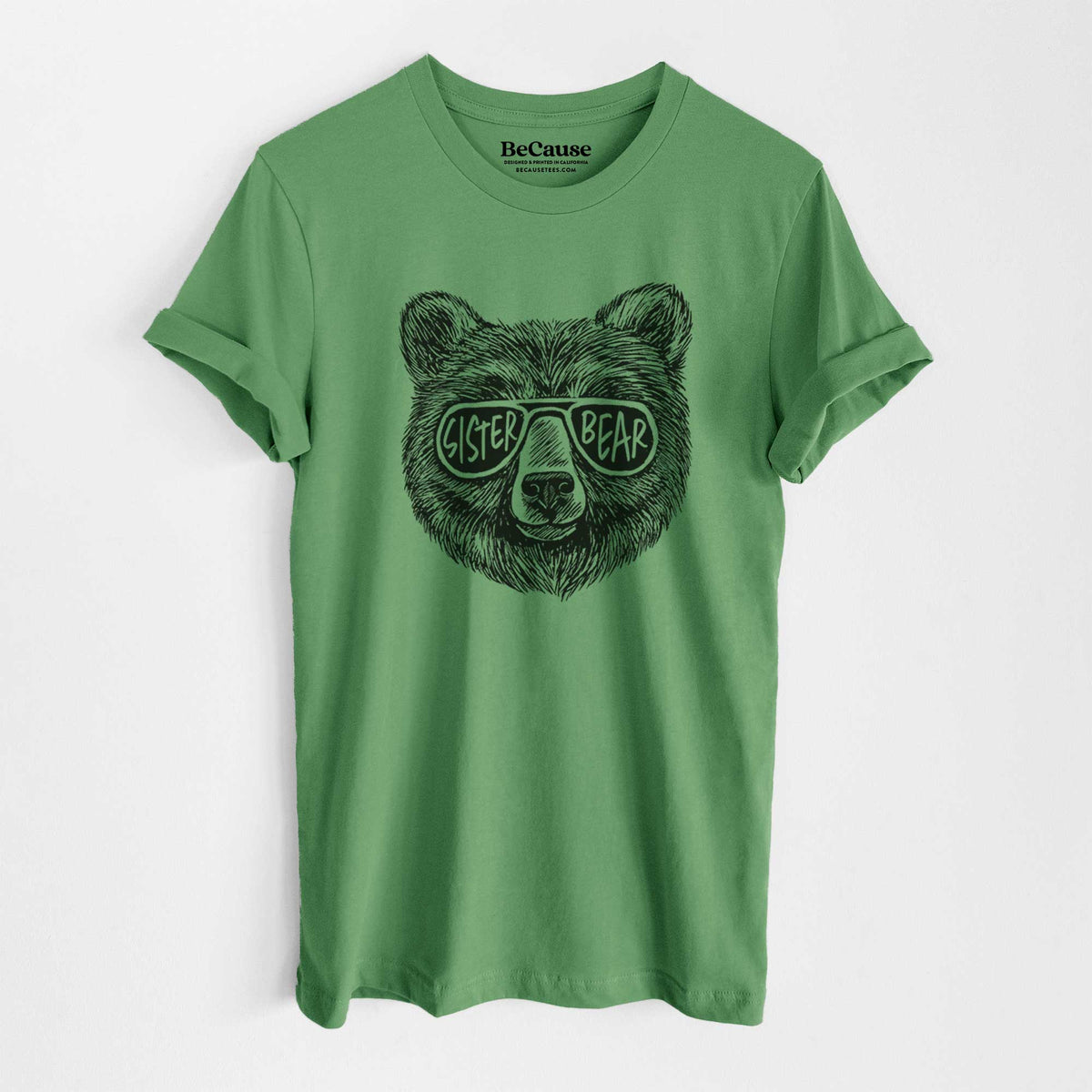 Leaf green lightweight cotton t-shirt laid flat, printed with a black ink bear's face wearing sunglasses that read Sister Bear.