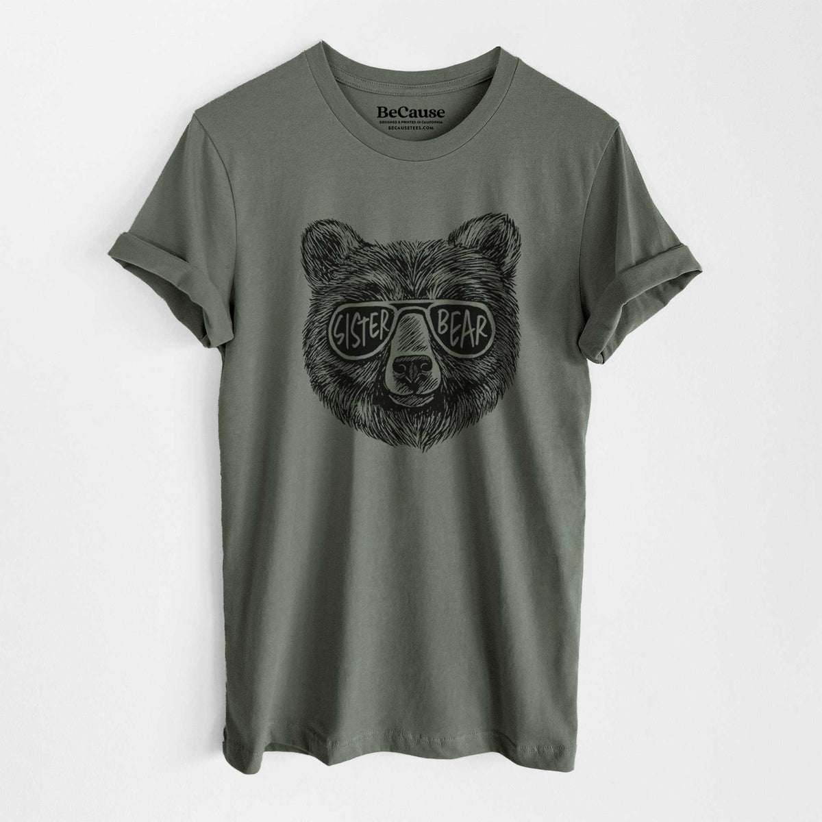 Military green lightweight cotton t-shirt laid flat, printed with a black ink bear's face wearing sunglasses that read Sister Bear.