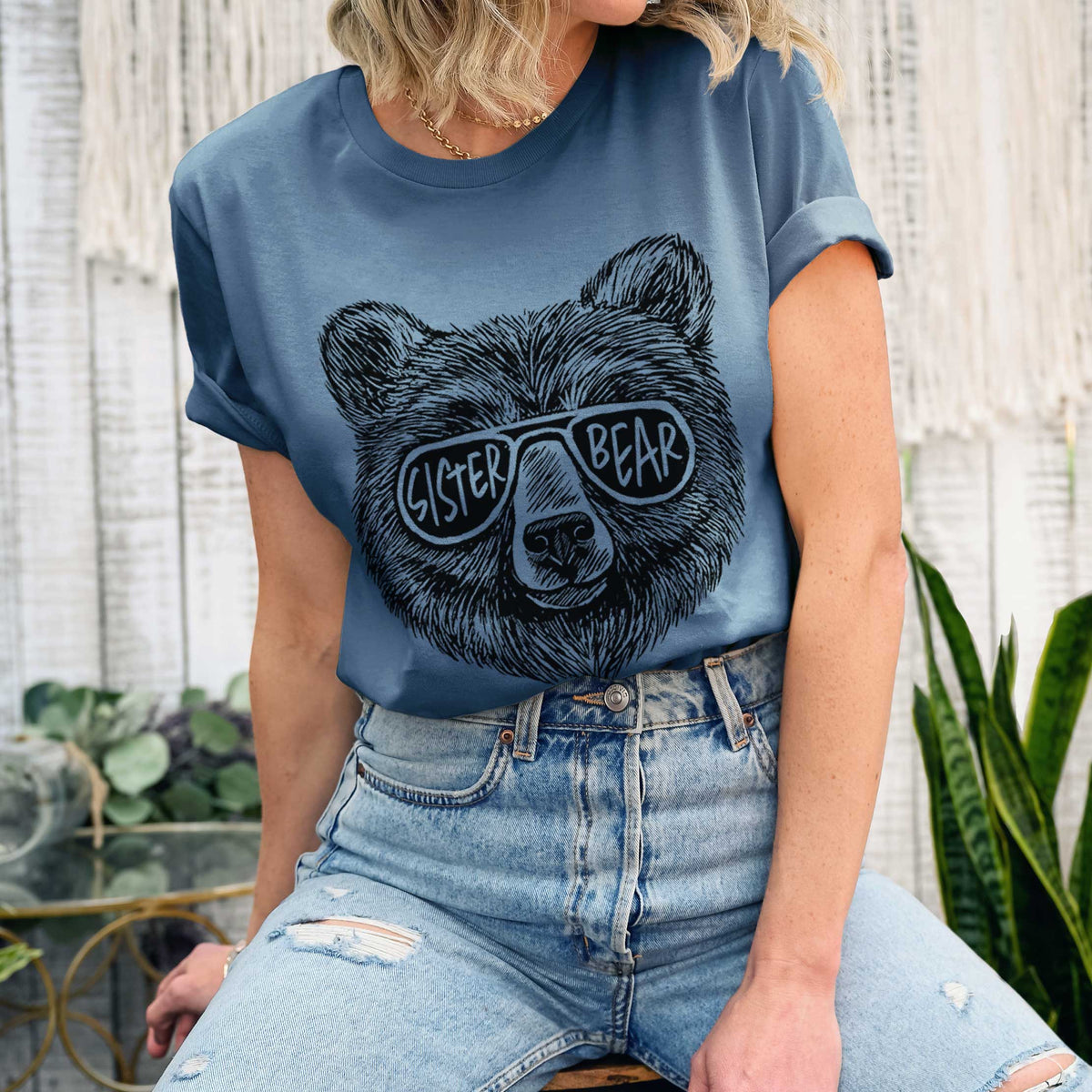 Woman wearing a steel blue lightweight cotton t-shirt printed with a black ink bear's face wearing sunglasses that read Sister Bear.