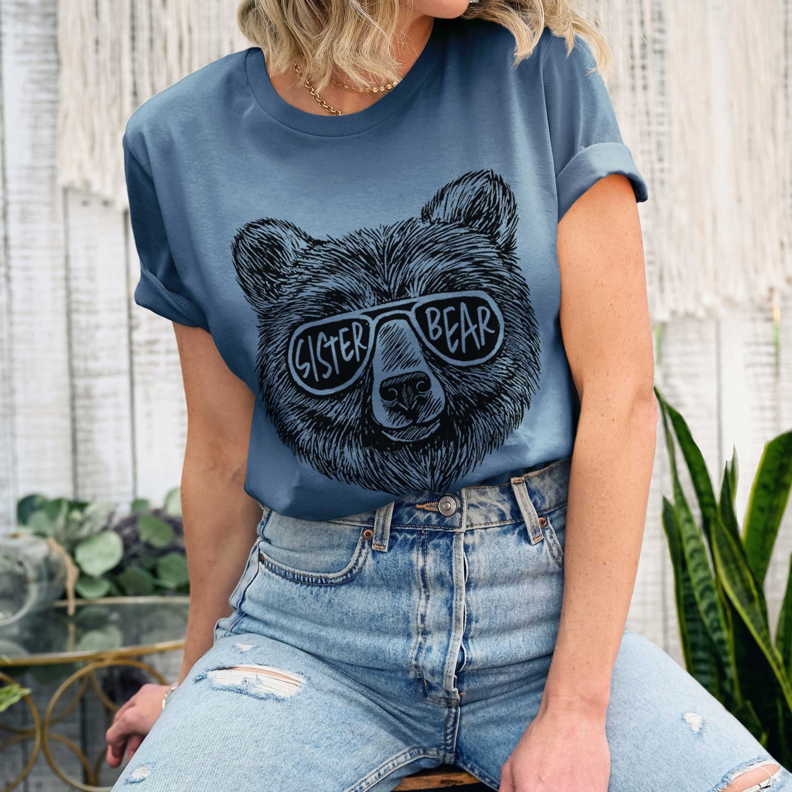 Mauve pink lightweight cotton t-shirt laid flat with the sleeves rolled, printed with a black ink bear's face wearing sunglasses that read Sister Bear.