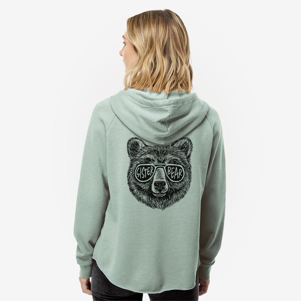 Woman wearing a sage green women's Cali Wave zip-up sweatshirt printed with a black ink bear's face wearing sunglasses that read Sister Bear, seen from behind.