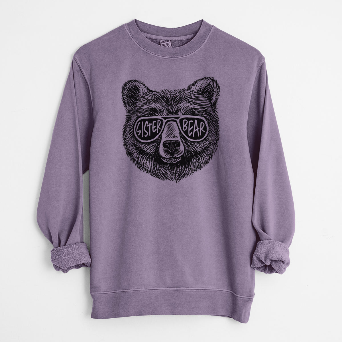 Plum purple pigment dyed crewneck sweatshirt laid flat with the sleeves rolled, printed with a black ink bear's face wearing sunglasses that read Sister Bear.