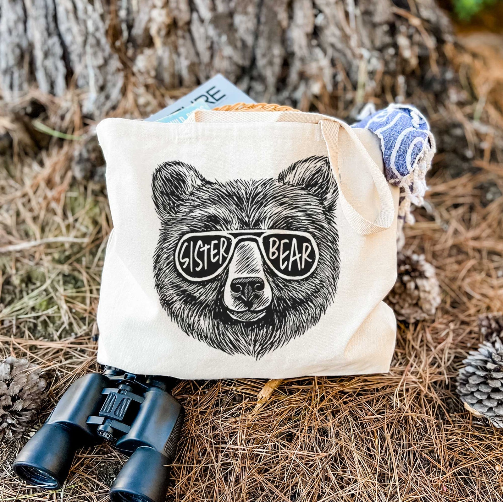 Natural canvas tote bag printed with a black ink bear's face wearing sunglasses that read Sister Bear.