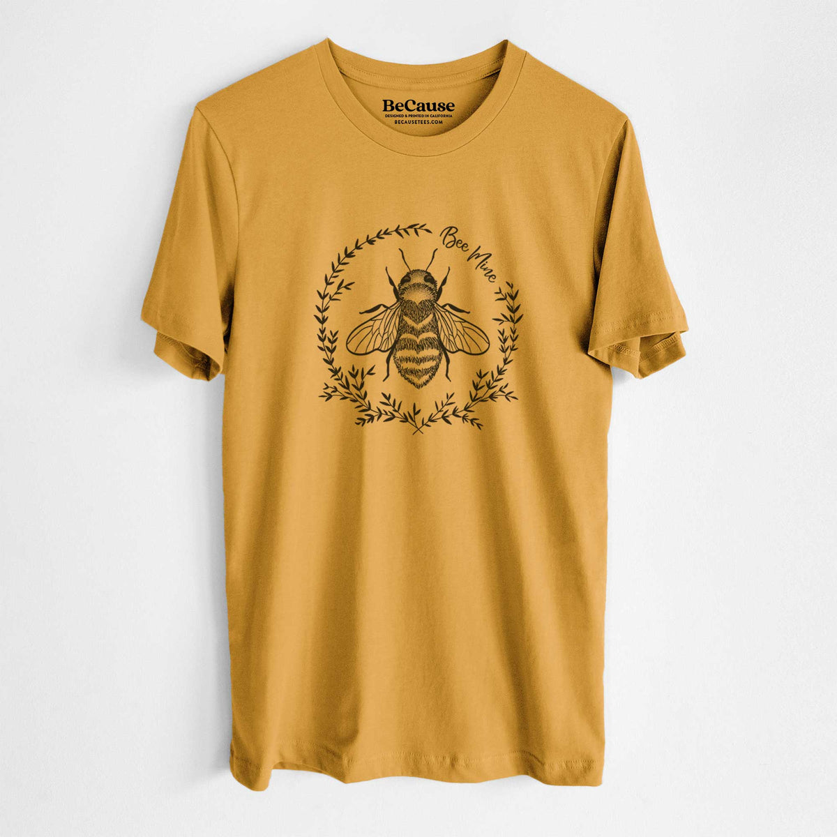 Mustard yellow lightweight cotton t-shirt laid flat, printed with a black ink bee inside a wreath of leaves with the words Bee Mine.