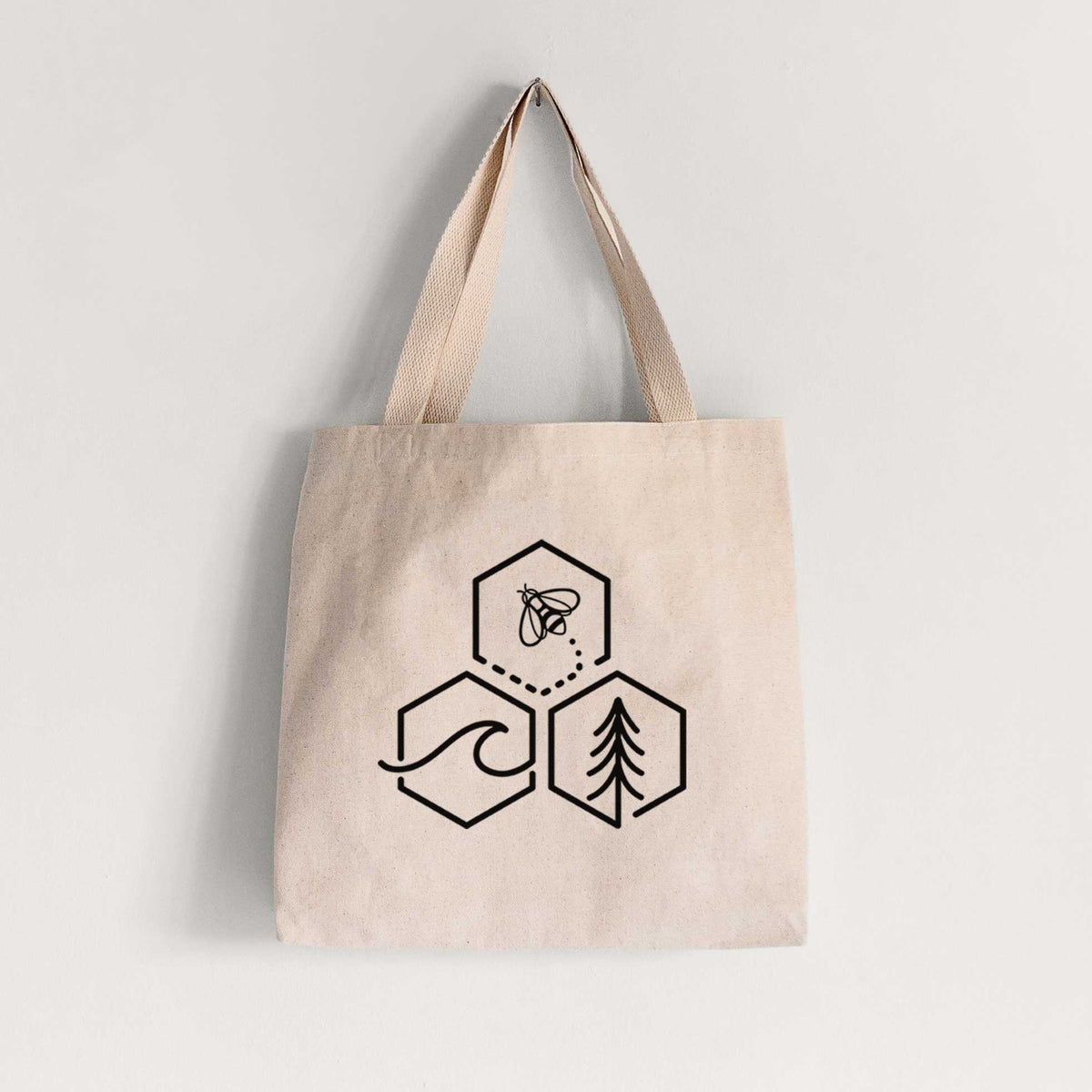 Natural canvas tote bag printed with a black line art design of three hexagons holding a bee, an ocean wave and a pine tree.