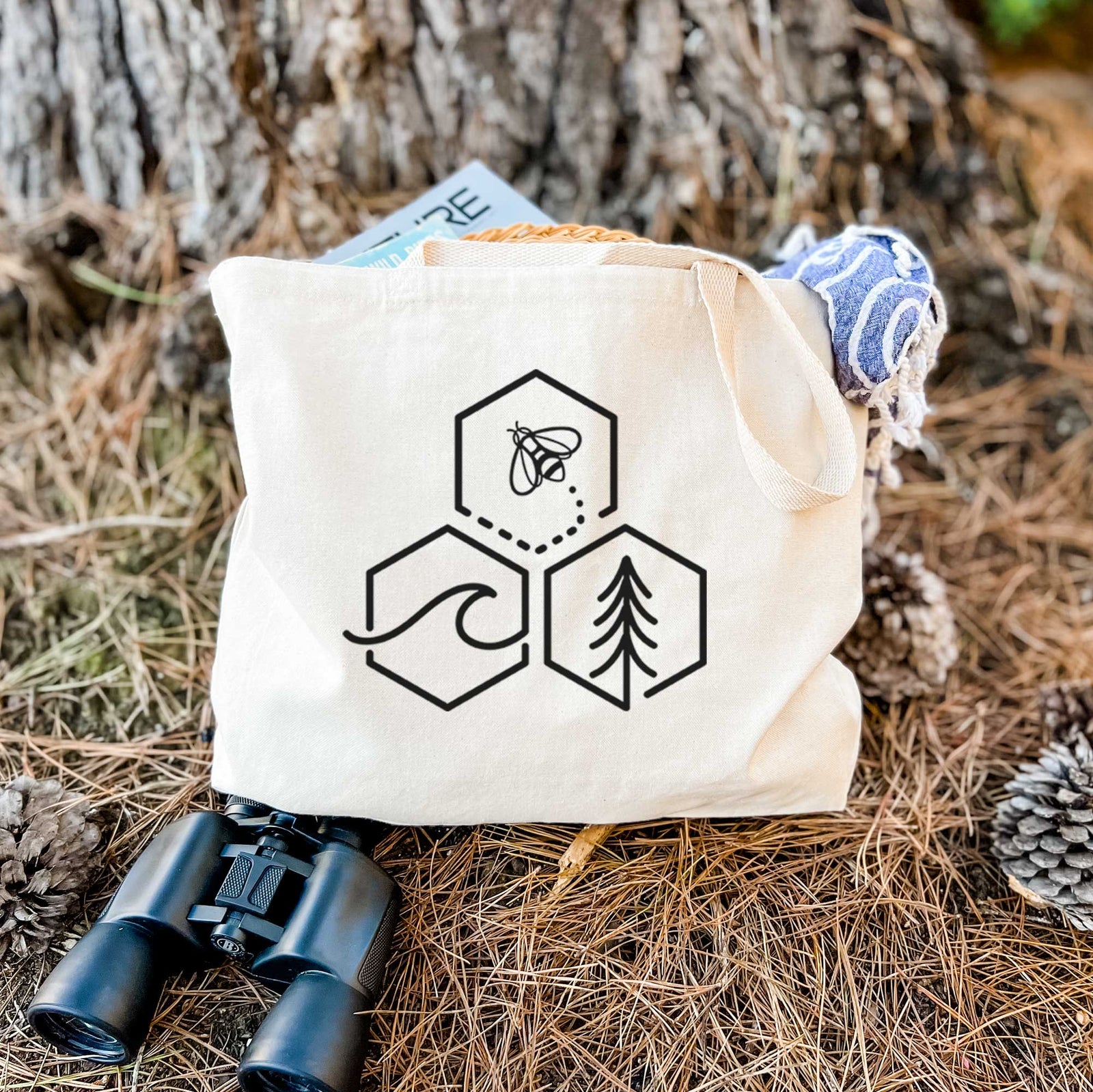 Natural canvas tote bag printed with a black line art design of three hexagons holding a bee, an ocean wave and a pine tree.