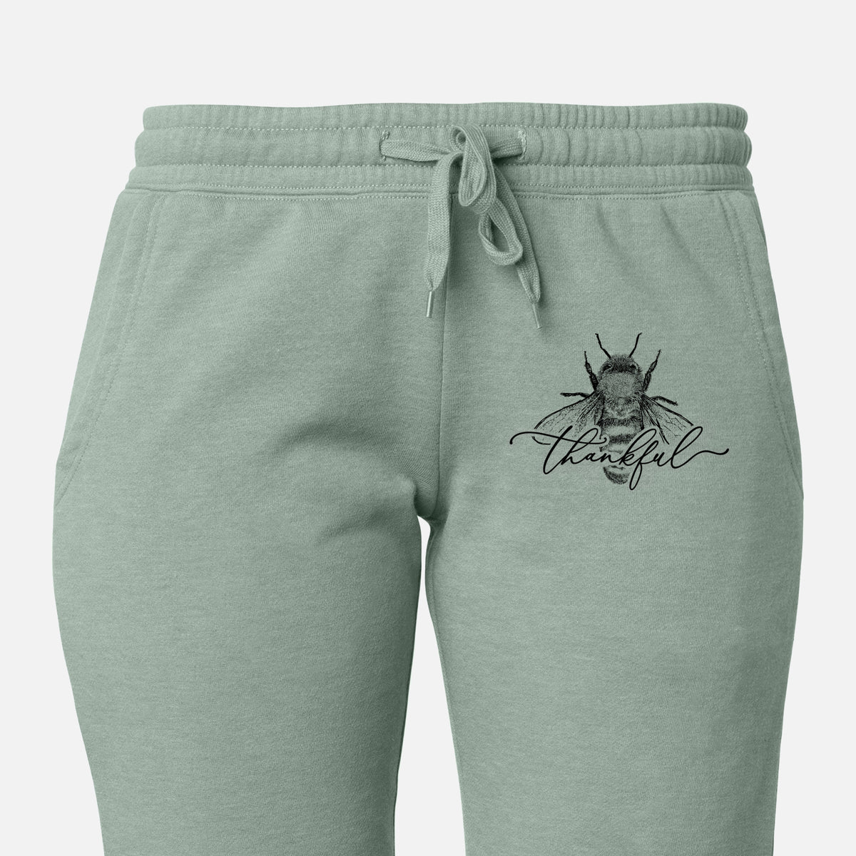 Front of sage green Cali Wave sweatpants, printed with a black ink bee with the word thankful written in script across it on the leg.