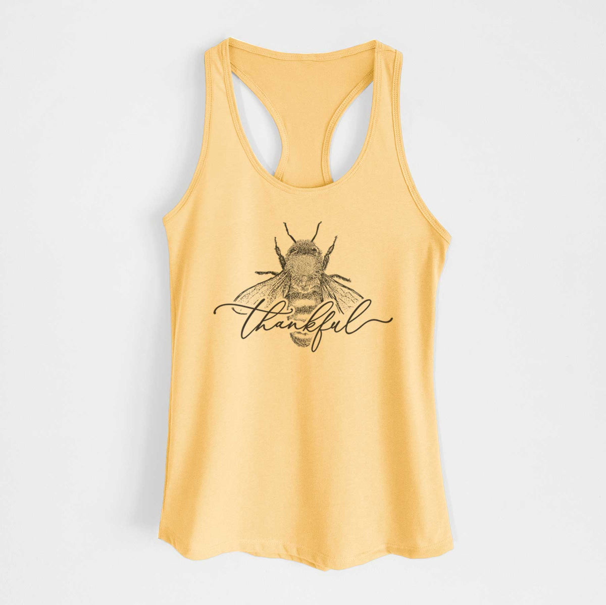 Banana cream women's racerback tank top laid flat, printed with a black ink bee with the word thankful written in script across it.
