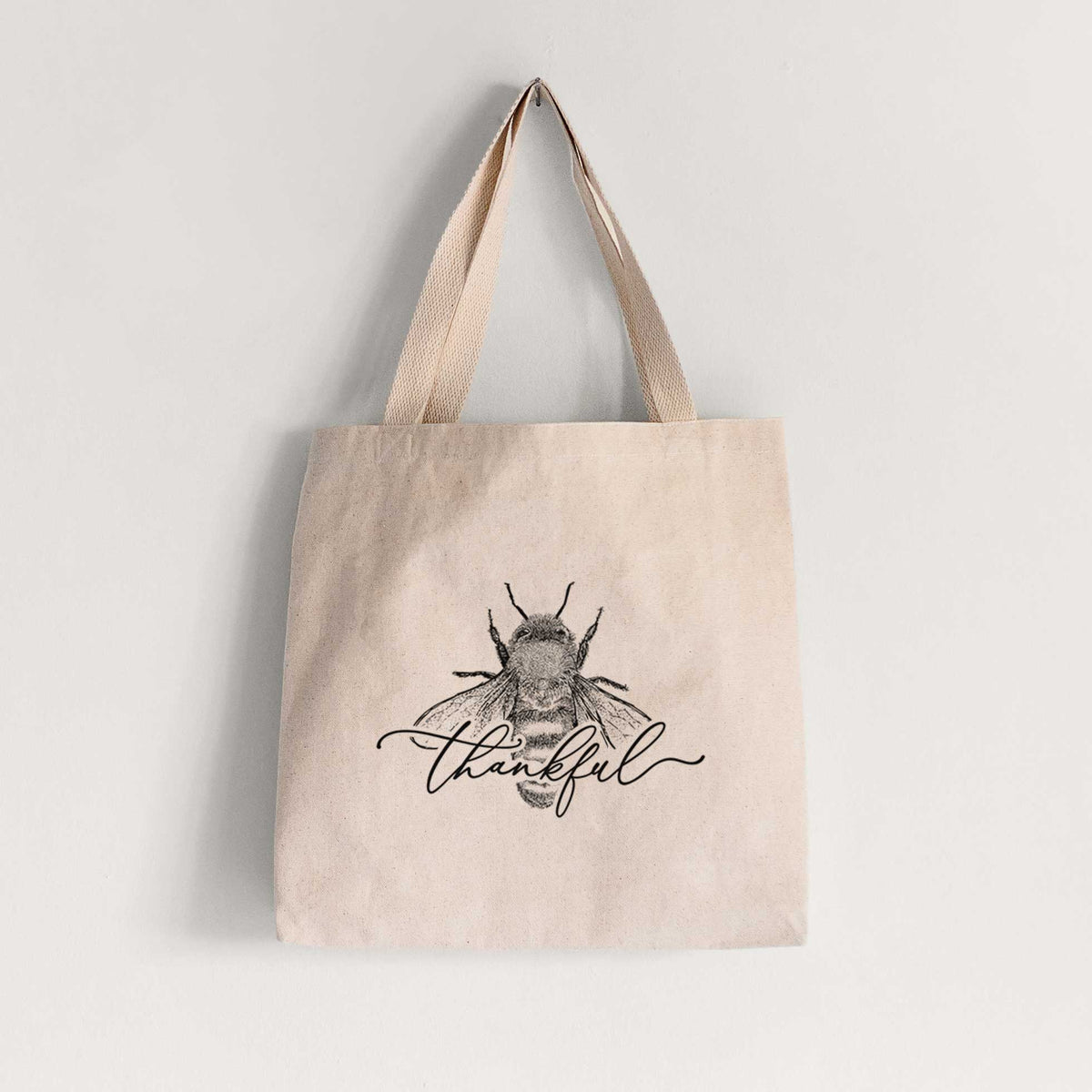 Natural canvas tote bag printed with a black ink bee with the word thankful written in script across it.