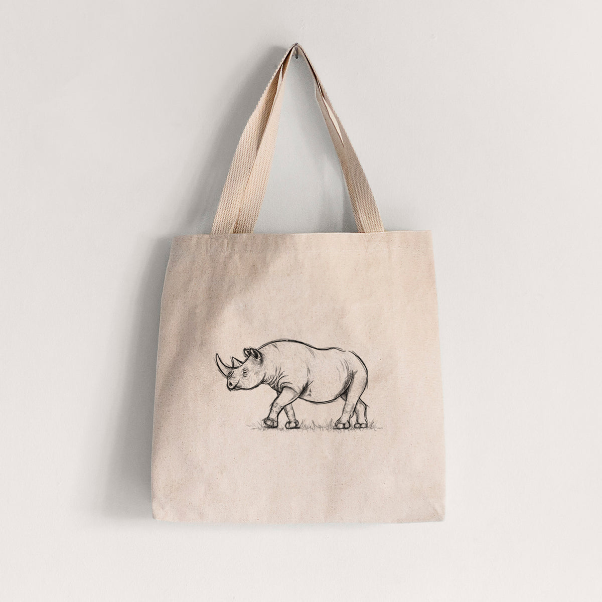 Natural canvas tote bag printed with a black ink illustration of a black rhinoceros walking.