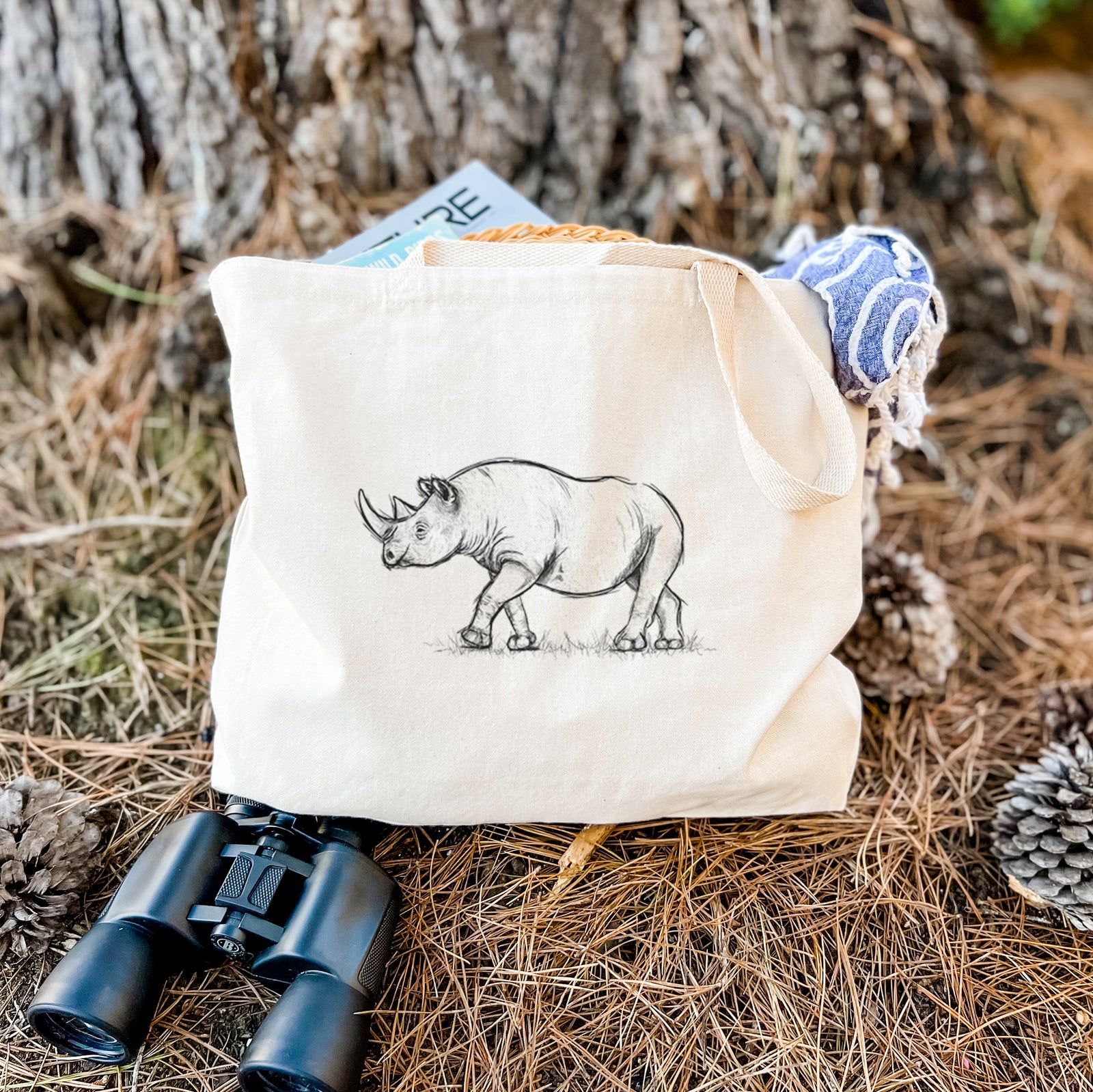 Natural canvas tote bag printed with a black ink illustration of a black rhinoceros walking.