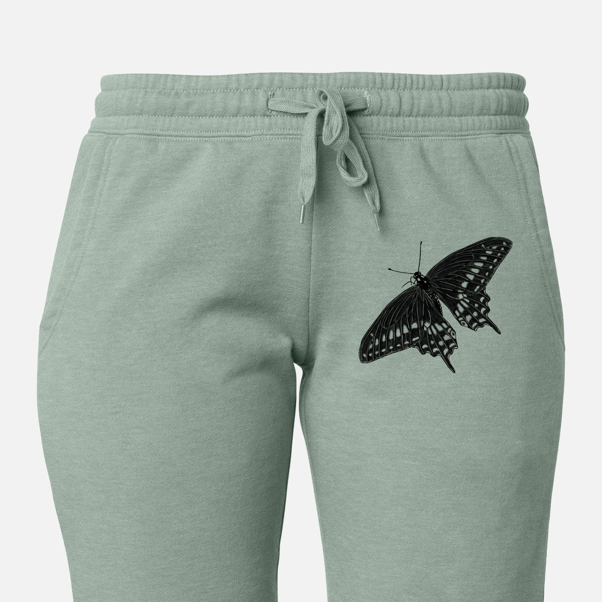 Front of sage green Cali Wave sweatpants, printed with a detailed black ink illustration of a black swallowtail butterfly with its wings spread on the leg.